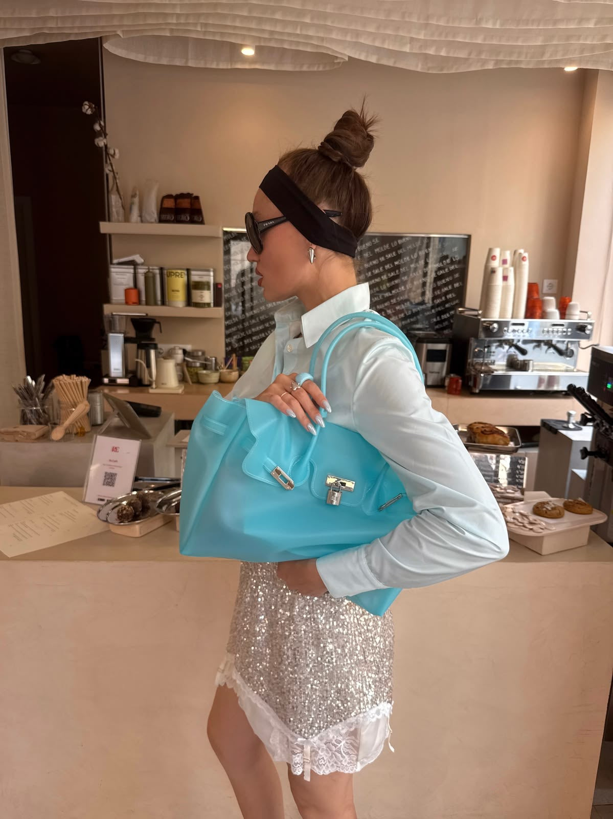 Cliente en chemise blanche tenant son sac Jelly Frosted bleu givré au comptoir d'un café, autre vue