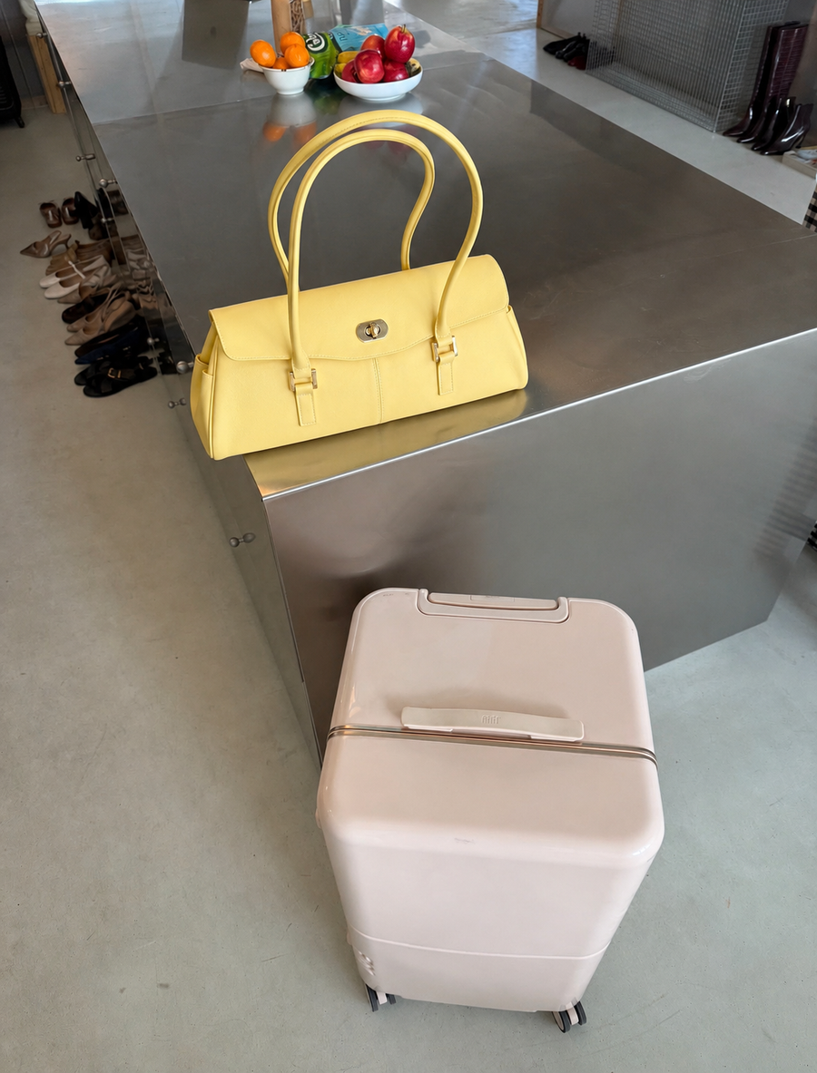 Sac baguette Jelly Firkin Butter jaune posé sur un plan de travail en cuisine, ambiance voyage avec valise beige