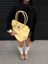 Sac Jelly Firkin Butter jaune beurre tenu à la main, porté avec un look automne-hiver casual chic