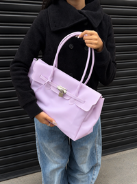 Mannequin tenant le sac Jelly Firkin Lilac violet contre lui, look manteau noir et jean baggy
