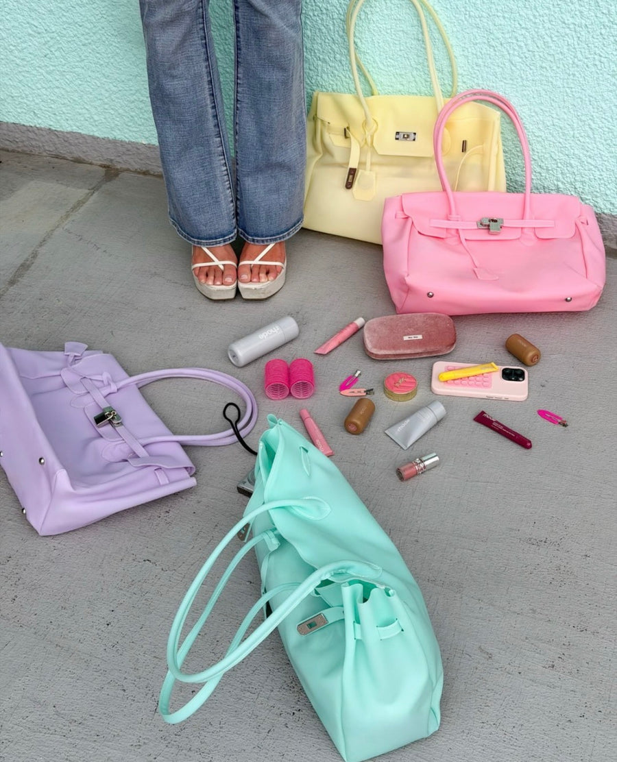 Mise en scène des sacs Jelly Firkin Butter jaune, Blush rose, Lilac violet et Mint vert menthe posés au sol avec accessoires