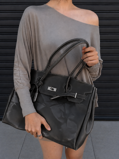 Mannequin tenant le sac Jelly Firkin Onyx noir à la main, look casual devant un rideau métallique
