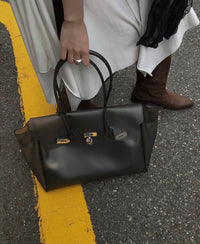 Sac Jelly Firkin Onyx noir tenu à la main par une femme en robe blanche et bottes, sur l'asphalte