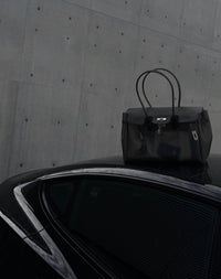 Sac Jelly Firkin Onyx noir posé sur le toit d'une voiture noire devant un mur en béton brut