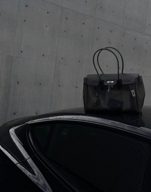 Sac Jelly Firkin Onyx noir posé sur le toit d'une voiture noire devant un mur en béton brut