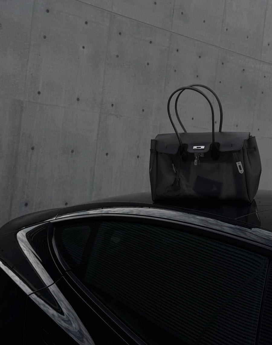 Sac Jelly Firkin Onyx noir posé sur le toit d'une voiture noire devant un mur en béton brut
